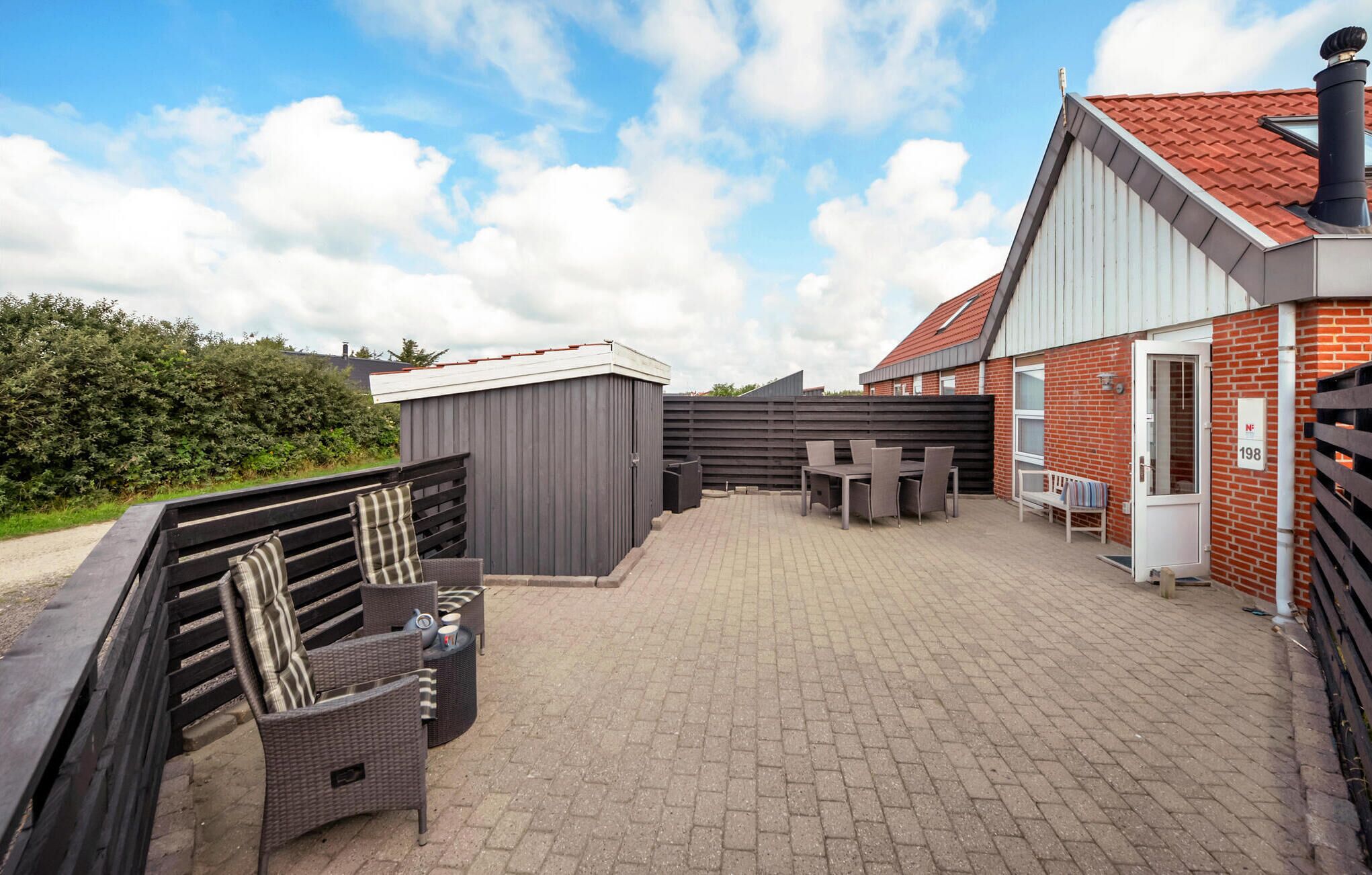 A patio area with outdoor furniture, a small shed, and a brick building with a red roof.