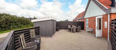 A patio area with outdoor furniture, a small shed, and a brick building with a red roof.