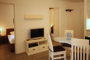 Una habitación con cama, televisor sobre un mueble, una mesa de comedor con sillas y un armario con cajones.