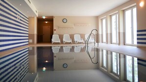 Een modern binnenzwembad met een spiegelende vloer, zitgelegenheid langs het zwembad en grote ramen voor natuurlijk licht.