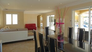 A spacious living room with a white sofa, a red armchair, and a dining area with a glass table and chairs.