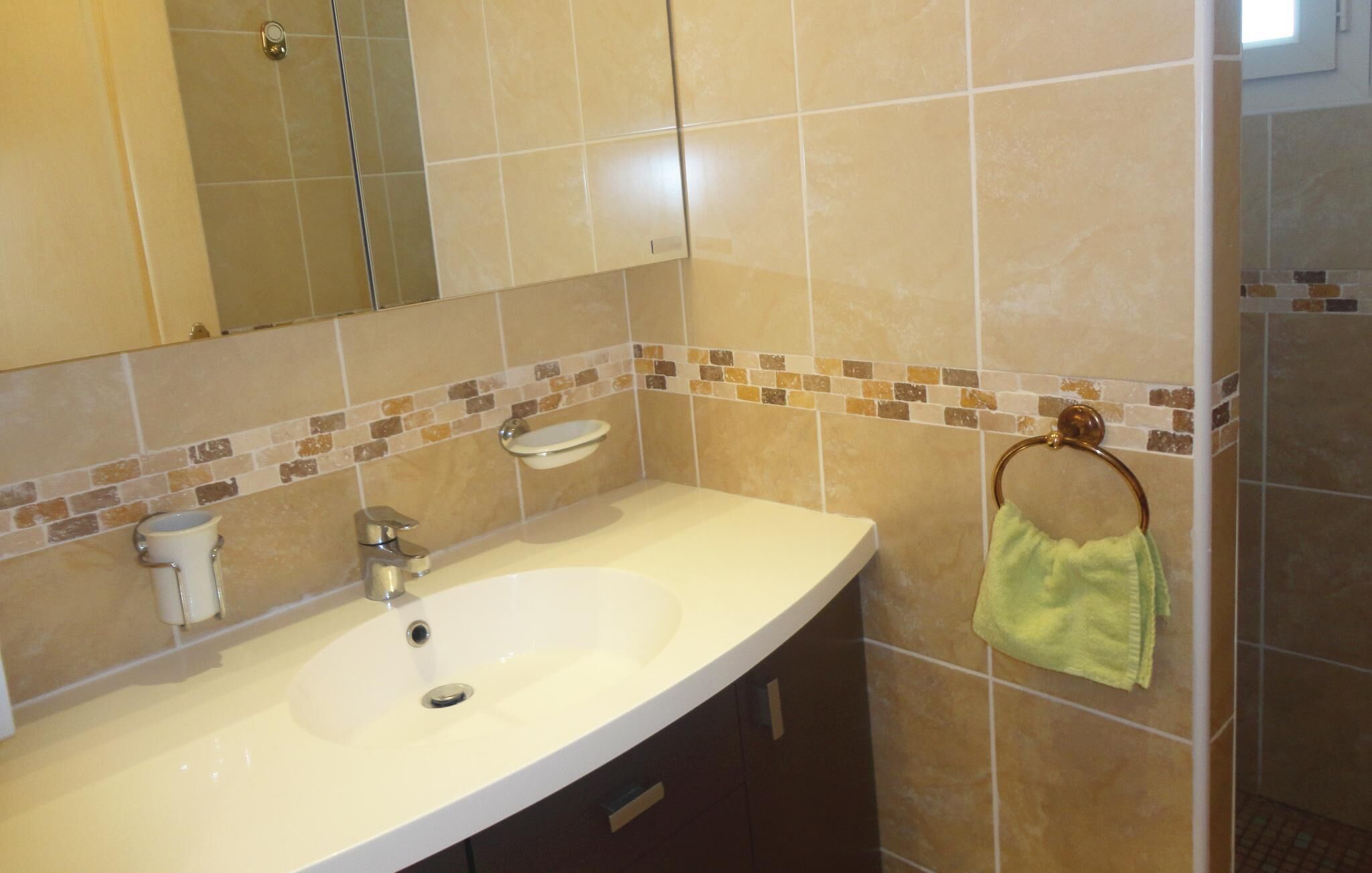 Une salle de bain avec un lavabo blanc, un miroir, un porte-serviettes avec une serviette et un pare-éclaboussures carrelé.