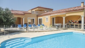 A poolside area with a clear blue pool, lounge chairs, and a building with a tiled roof and yellow walls.