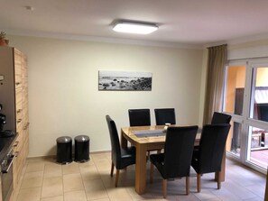 Ein Essbereich mit einem Holztisch und schwarzen Stühlen, einer schwarzen Mülltonne und einem Schwarz-Weiß-Foto an der Wand.