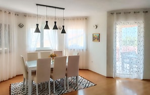 A dining area with a table and chairs, pendant lights, a patterned rug, and a window with sheer curtains.