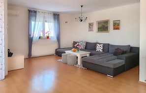 A modern living room with a grey sectional sofa, a white coffee table, and a window with sheer curtains.
