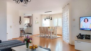 Un soggiorno con un divano, un tavolino da caffè con un vaso e una ciotola di frutta, una TV e un'area pranzo con sedie e un tavolo.