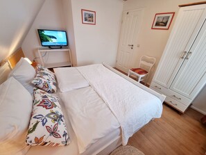 A bedroom with a bed, a TV, a chair, and a wardrobe.