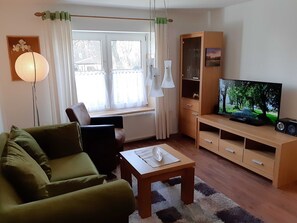 A living room with a sofa, a coffee table, a TV on a wooden stand, and a cabinet.