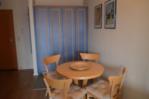 Ein Essbereich mit einem runden Holztisch, vier Stühlen, einem blauen Kleiderschrank und zwei gerahmten Bildern an der Wand.