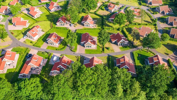 Vue aérienne d’un quartier résidentiel, avec des maisons aux toits rouges, entourées de pelouses verdoyantes et d’arbres.