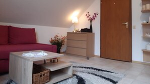 Un salón acogedor con un sofá rojo, una mesa de centro de madera, una lámpara y un florero con flores.