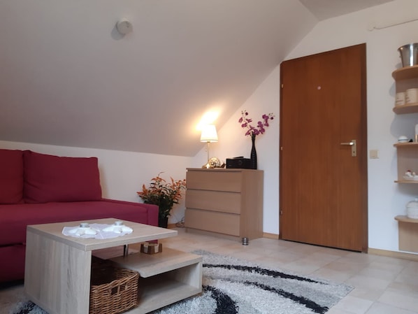 A cozy living room with a red sofa, a wooden coffee table, a lamp, and a vase with flowers.