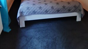 Una habitación pequeña con cama individual, una colcha estampada de estrellas, dos lámparas de noche y una luz en el techo.