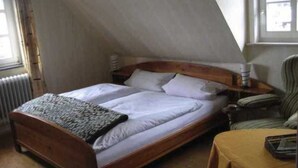 Un letto singolo in una stanza con soffitto spiovente, un termosifone, una sedia e un tavolo.