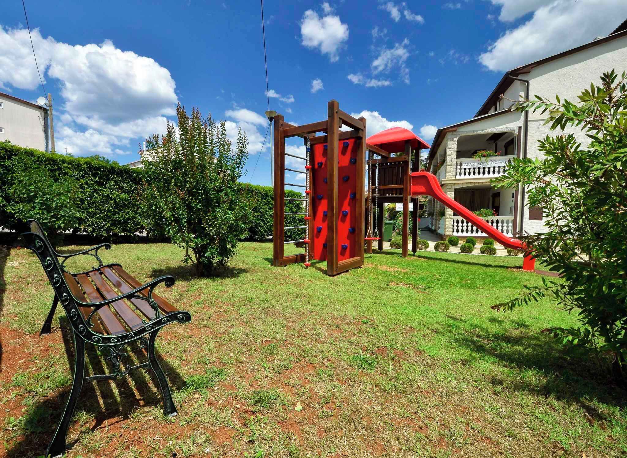 A playground with a slide and climbing structure, a bench, and a building in the background.