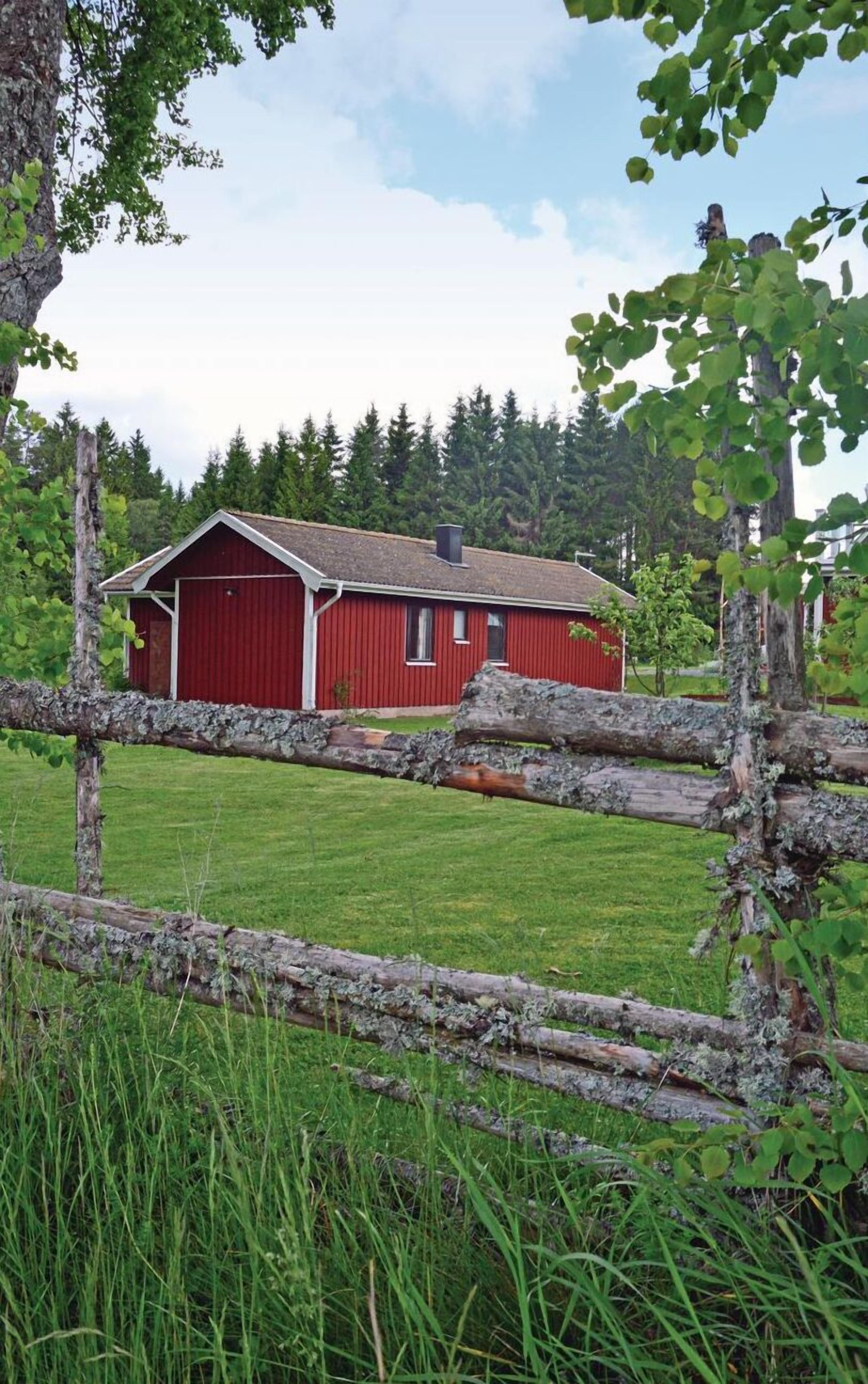 Une grange rouge avec une porte et des fenêtres blanches, entourée d’une clôture en bois et d’une pelouse verdoyante.