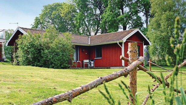 A red wooden house with a tiled roof, surrounded by a grassy lawn and trees.