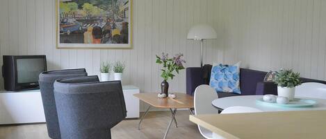 Een moderne woonkamer met een bank, stoelen, een bijzettafeltje en een televisie.