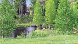 A serene pond surrounded by lush greenery and a small building in the background.