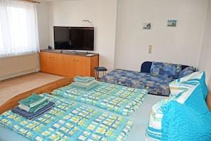 A bedroom with a TV, two beds, a sofa, and a window with curtains.