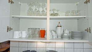 A kitchen with white cabinets, two shelves with glassware, and a coffee maker.
