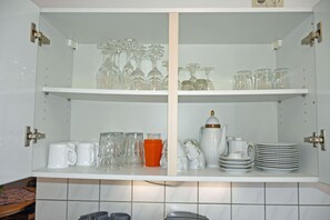 A kitchen with white cabinets, shelves with glassware, mugs, and plates.
