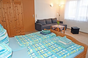 A bedroom with a bed, a sofa, a small table with a vase, and a speaker.