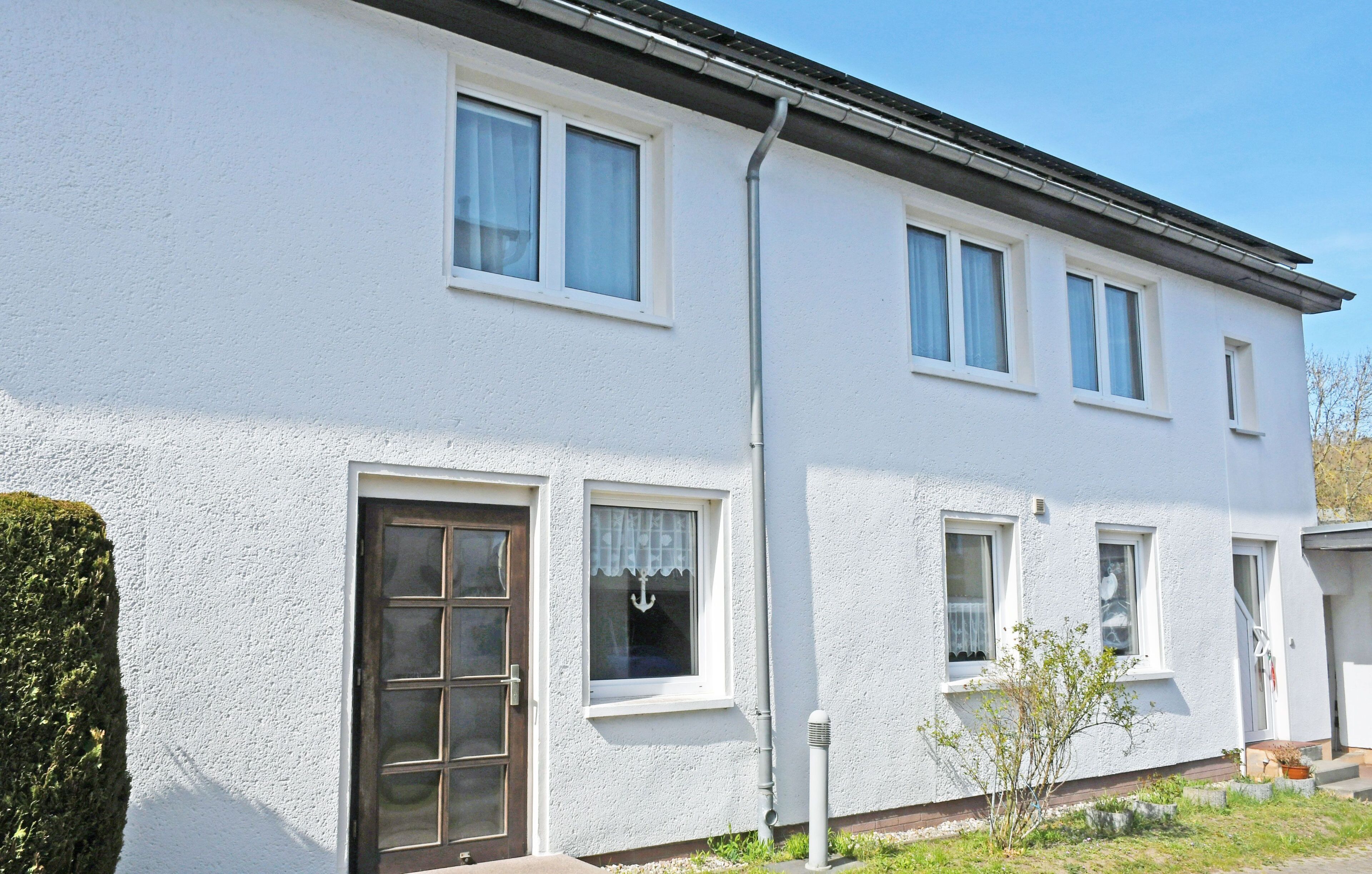 A white two-story house with a front door, windows, and a small garden.