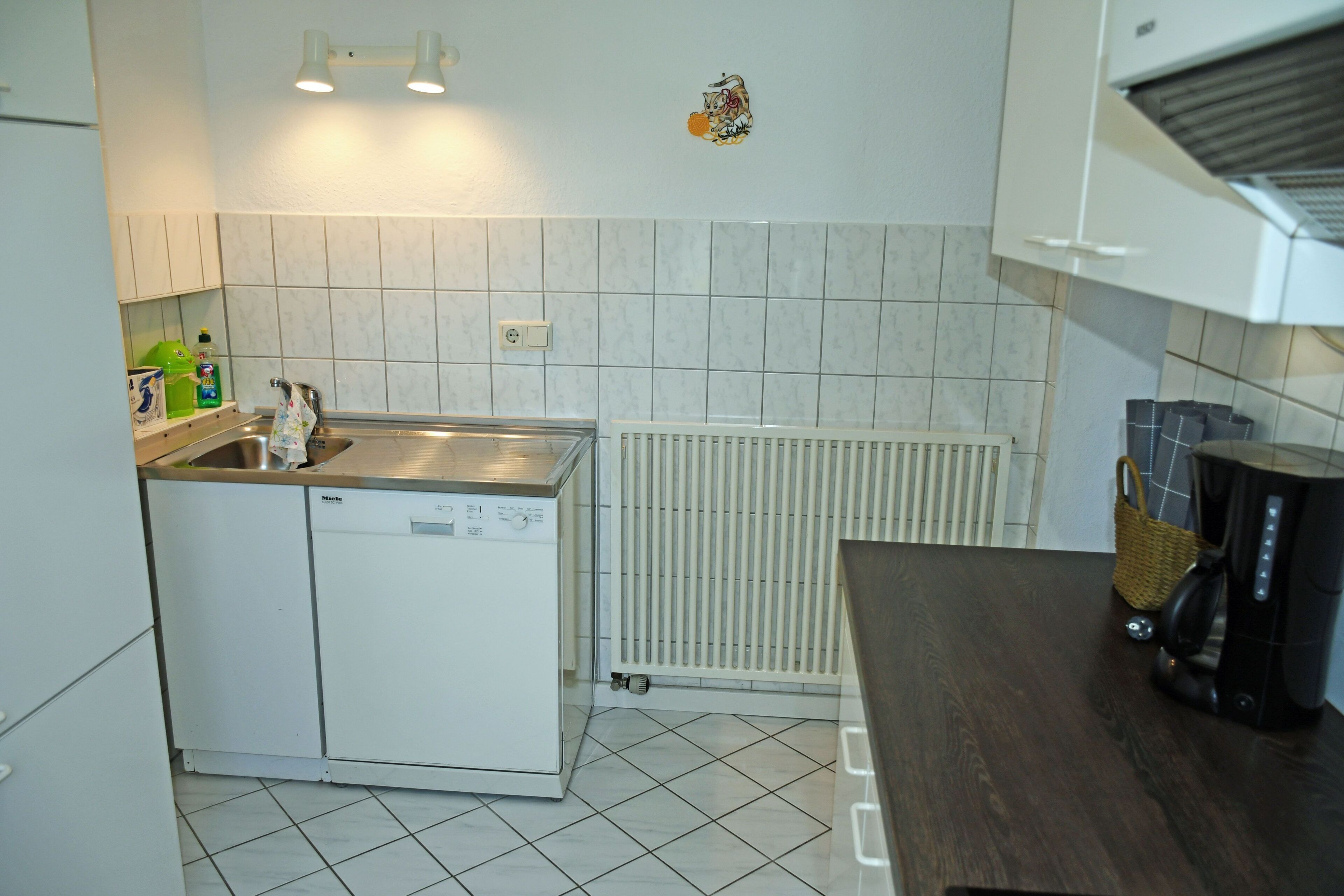 Kompakti keittiö, jossa on astianpesukone, vedenkeitin ja kahvinkeitin työtasolla.