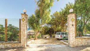 A gated entrance with stone pillars and a chain-link fence, leading to a parking area with a white van.