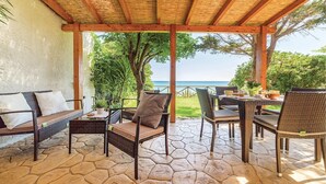A covered outdoor seating area with wicker furniture and a stone floor, overlooking a scenic view.