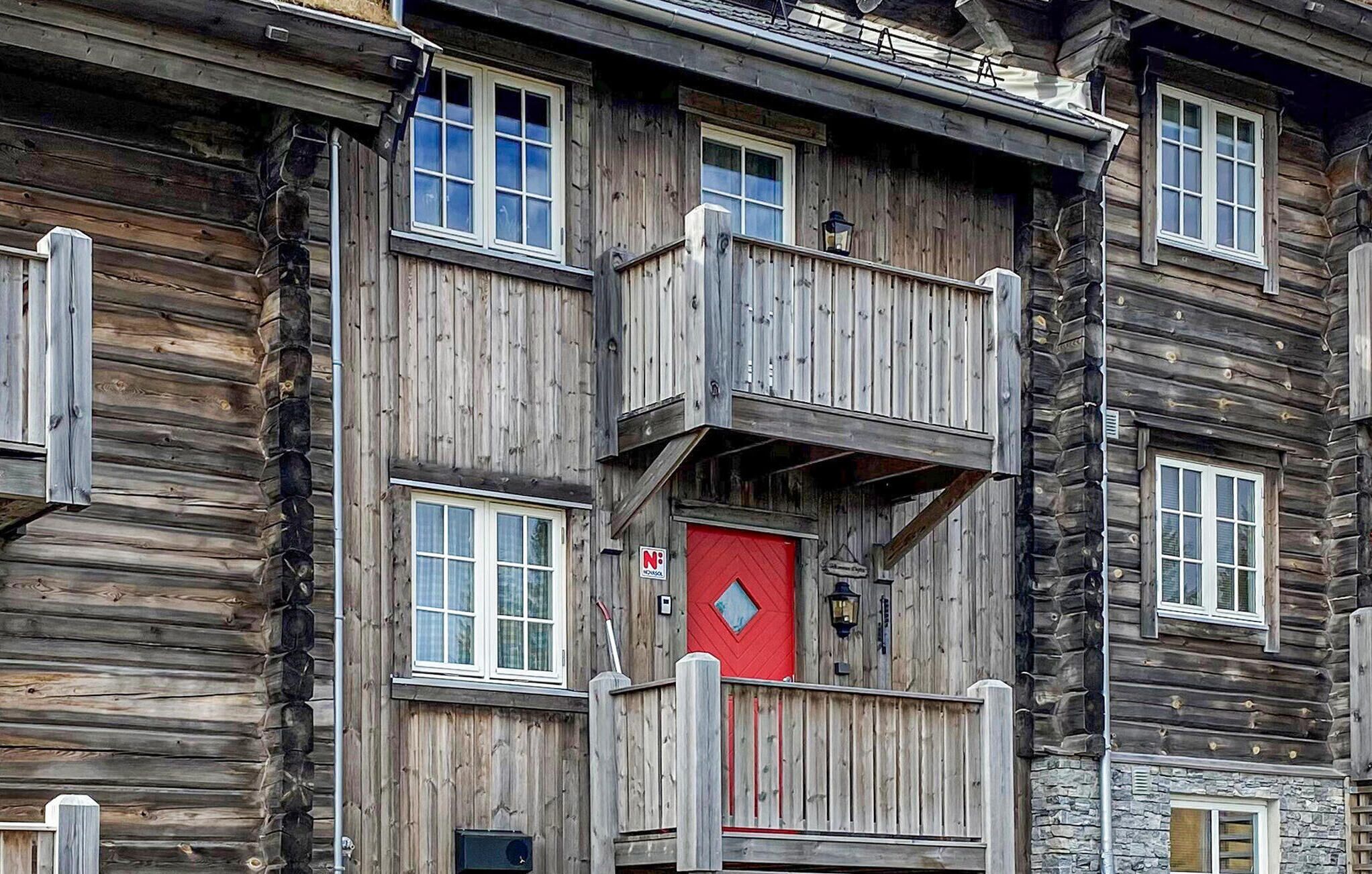Un edificio de madera de varios pisos, con balcones, una puerta roja y un letrero que indica una escuela.