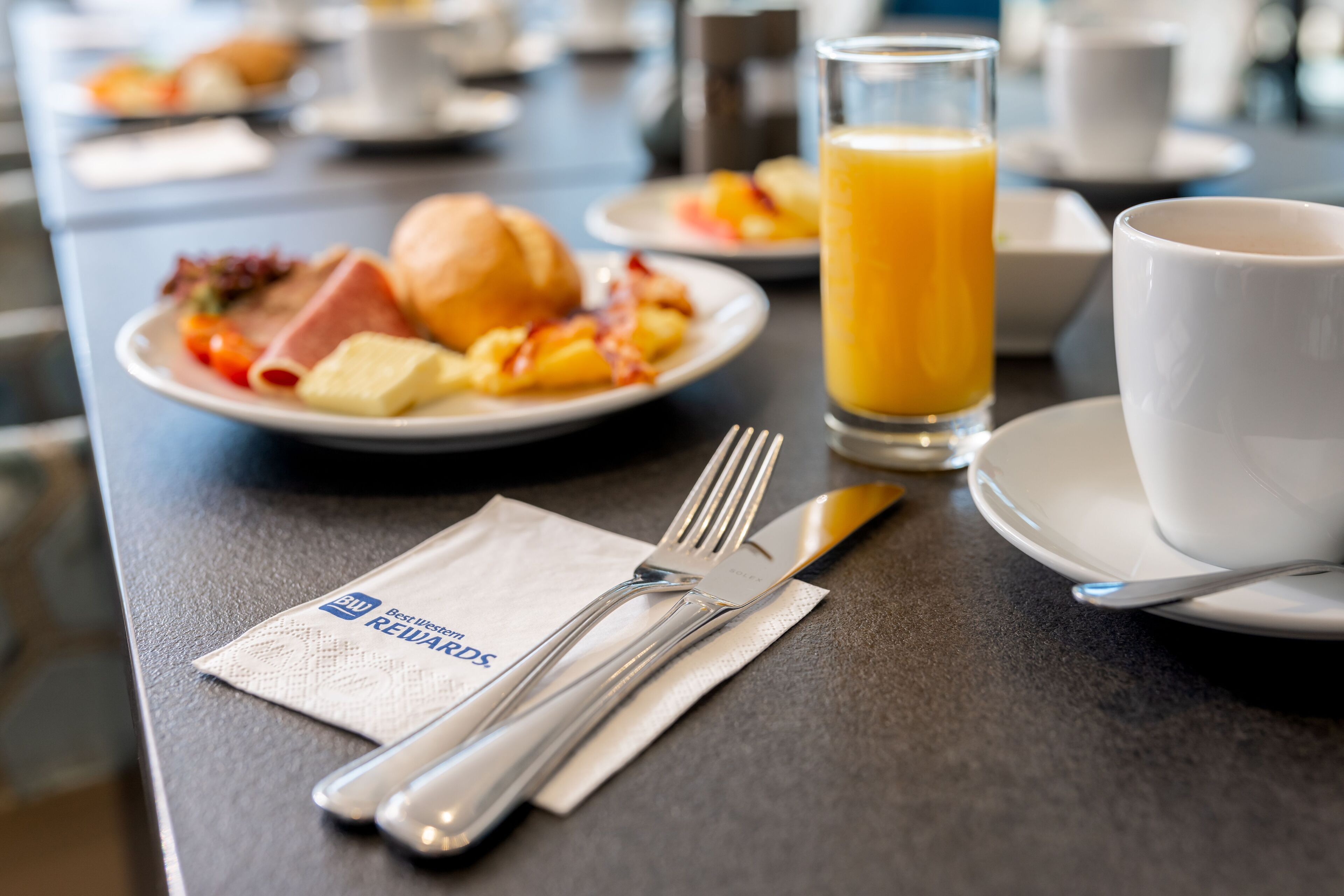 A breakfast setting with plates of food, a glass of orange juice, and a cup and saucer on a table.