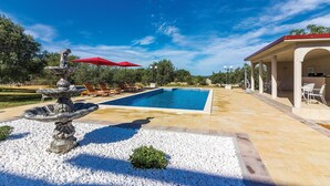 Una piscina con fuente, tumbonas y un área de patio techada.