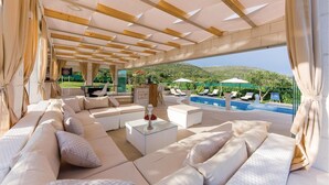 Un vaste espace de détente extérieur avec piscine, des sièges confortables et une vue sur les collines.