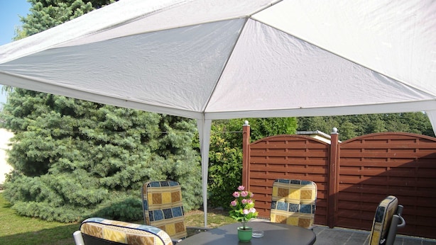 Ein Patio mit Tisch und Stühlen unter einer weißen Markise, umgeben von einem Holzzaun und Grünpflanzen.