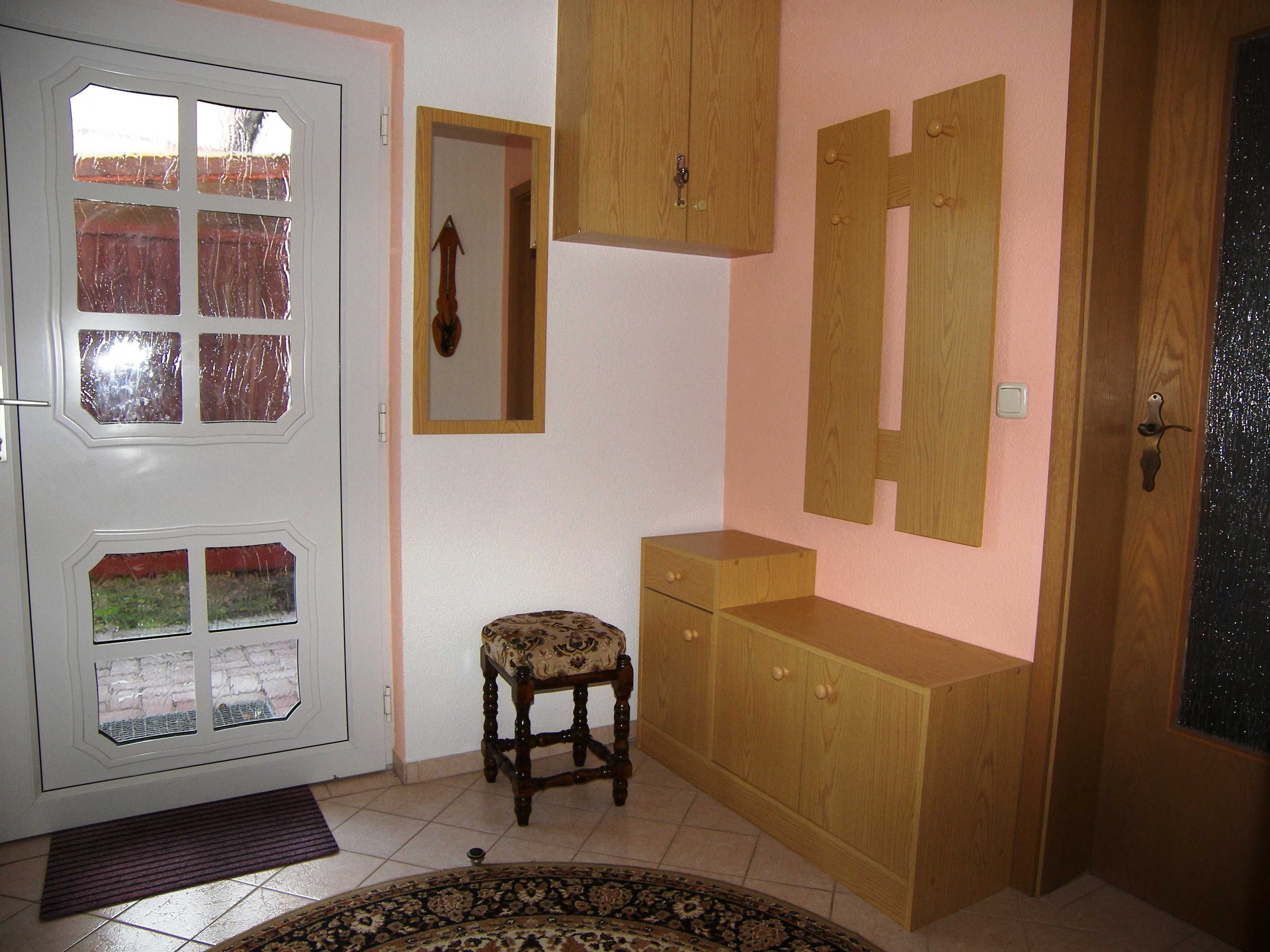 Una habitación con una puerta blanca con paneles de vidrio, una pequeña silla de madera, un armario de madera y un espejo en la pared.