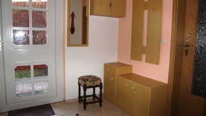 Ein Zimmer mit einer weißen Tür, Glaseinsätzen, einem kleinen Holzstuhl, einem Holzschrank und einem Spiegel an der Wand.