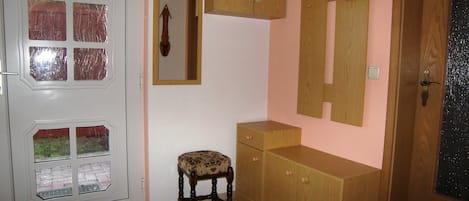 Una habitación con una puerta blanca con paneles de vidrio, una pequeña silla de madera, un armario de madera y un espejo en la pared.