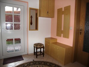 A room with a white door with glass panels, a small wooden chair, a wooden cabinet, and a mirror on the wall.