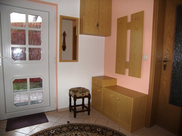 Ein Zimmer mit einer weißen Tür, Glaseinsätzen, einem kleinen Holzstuhl, einem Holzschrank und einem Spiegel an der Wand.