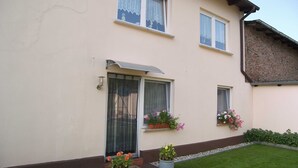 Ein zweistöckiges Gebäude mit flachem Dach, einer kleinen Veranda und einem Ziegelteil auf der rechten Seite.