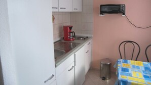 Eine kleine Küche mit weißen Schränken, einer roten Kaffeemaschine, einer Mikrowelle und einem Mülleimer.