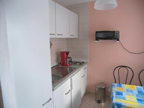 A small kitchen with white cabinets, a red coffee maker, a microwave, and a trash can.