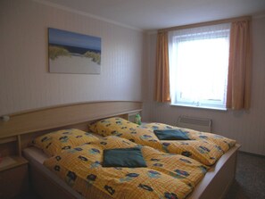 Ein Schlafzimmer mit Bett, einem Fenster mit Vorhängen, einem Bild an der Wand und einem Heizkörper.