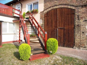 Eine Treppe mit roten Geländern führt zu einem Gebäude mit einer großen Holztür und einer Backsteinmauer.