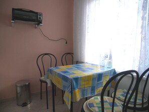 Ein kleiner Essbereich mit einem Tisch, der mit einer blau-gelben Tischdecke bedeckt ist, zwei Stühlen, einem Mülleimer und einem an der Wand befestigten Radio.