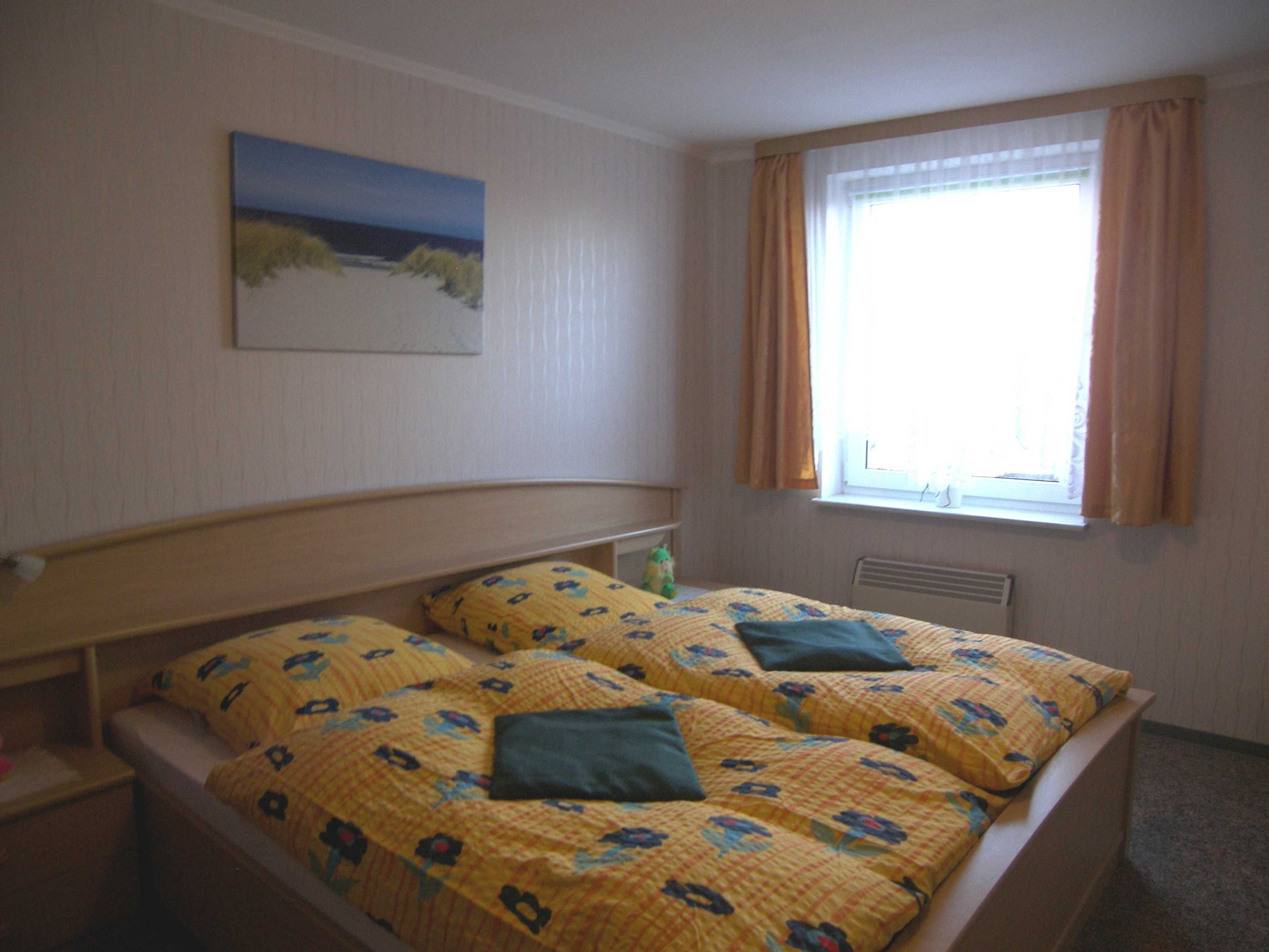 Ein Schlafzimmer mit Bett, einem Fenster mit Vorhängen, einem Bild an der Wand und einem Heizkörper.