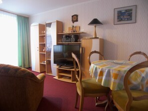 Ein Wohnzimmer mit Fernseher, Holzschrank und Esstisch mit Stühlen.
